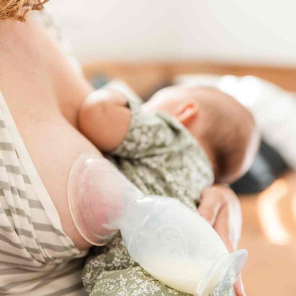 Mamá alimentando a su bebé mientras recoge la leche del pecho contario al que amamanta con un recolector con base de succión de leche materna Haakaa. El recolector de Haakaa aprovecha el reflejo de eyección y mediante una succión pasiva recoge la leche que de otro modo se perdería en un disco de lactancia. Fabricado 100% de silicona de alta calidad.